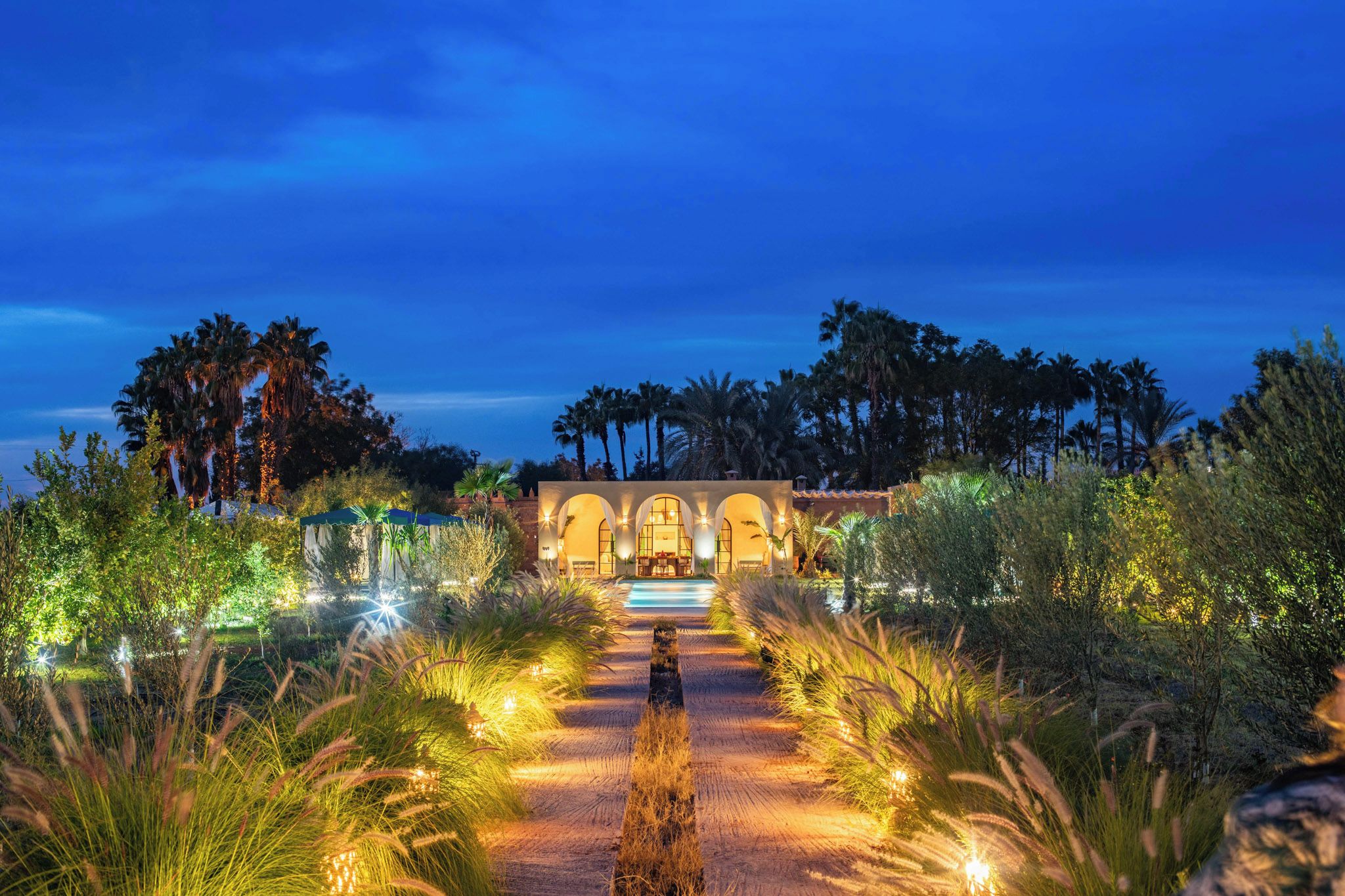 A pathway leading to a building with arched windows and a pool.