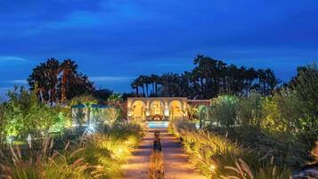 A pathway leading to a building with arched windows and a pool.