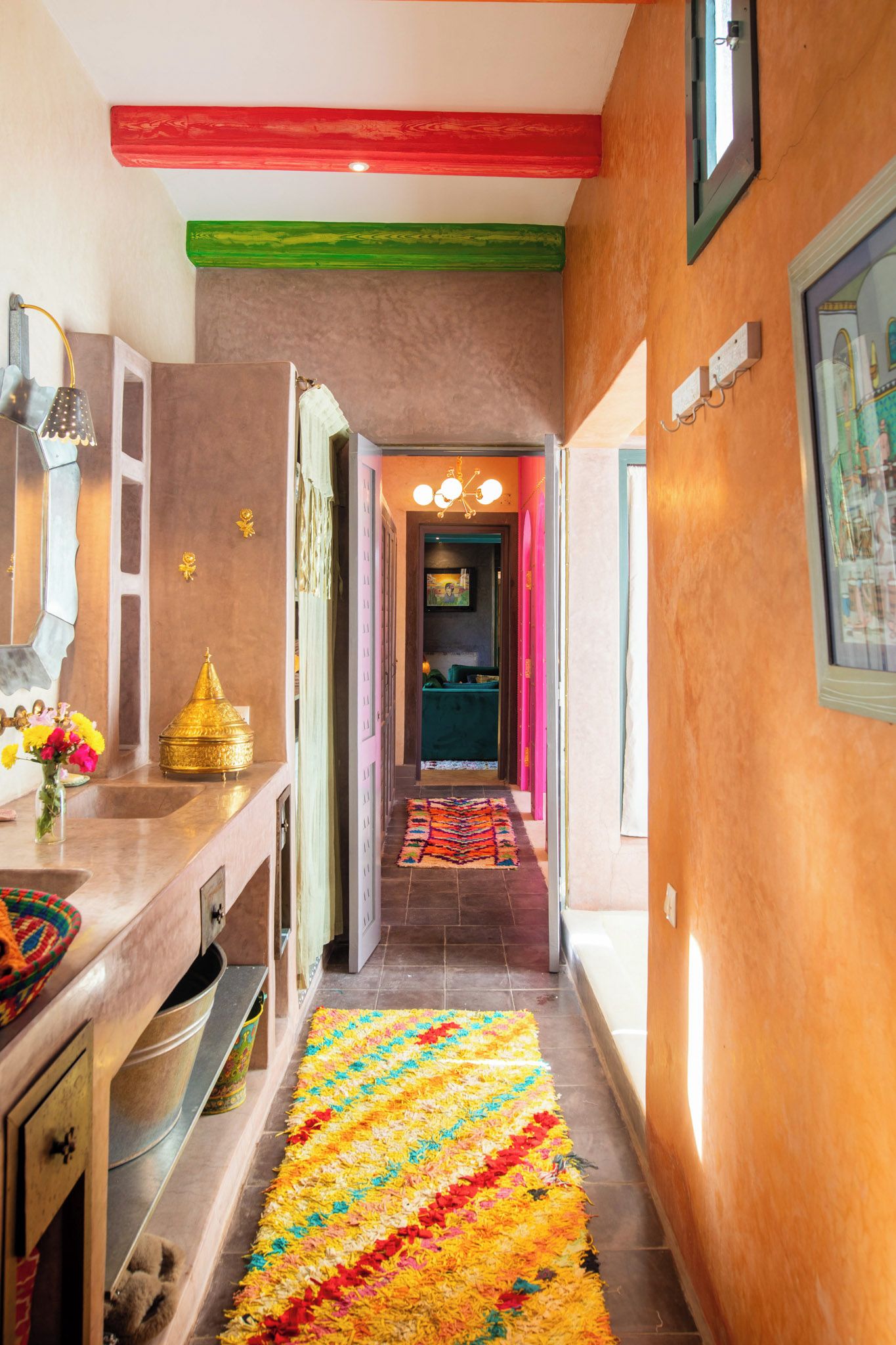Un couloir avec une moquette colorée, un lavabo et un miroir sur le côté gauche.