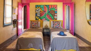 Une chambre d’hôtel avec deux lits, une fresque murale colorée et une petite table avec une lampe.