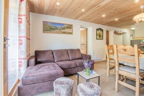Ein gemütliches Wohnzimmer mit einer braunen Eckcouch, einem kleinen Tisch mit einer Blumenvase und einem Essbereich mit Holzsesseln und einem Tisch.