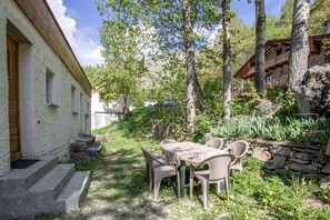 Ein Steinhaus mit einem Holzbalkon, umgeben von Bäumen und einem Garten mit Tisch und Stühlen.