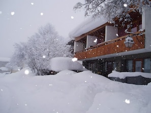 Ein zweistöckiges Gebäude mit einem hölzernen Balkon und schneebedeckten Bäumen.