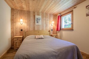 Ein Schlafzimmer mit Holzwänden, einem Bett, Nachttischen und einem Fenster mit Vorhängen.
