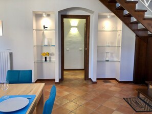A dining area with a wooden table and chairs, a glass shelf with decorative items, and a staircase in the background. - PALAZZO PRINCIPE - In the heart of STRESA! (Stresa)