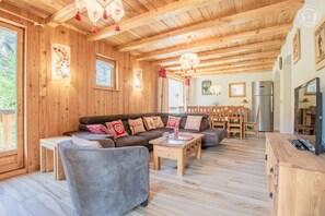 A wooden interior with a sofa, ottoman, and a dining area with chairs and a table. - Apartment 'La Pastourelle 1' with Balcony and Wi-Fi (Bonneval-sur-Arc)