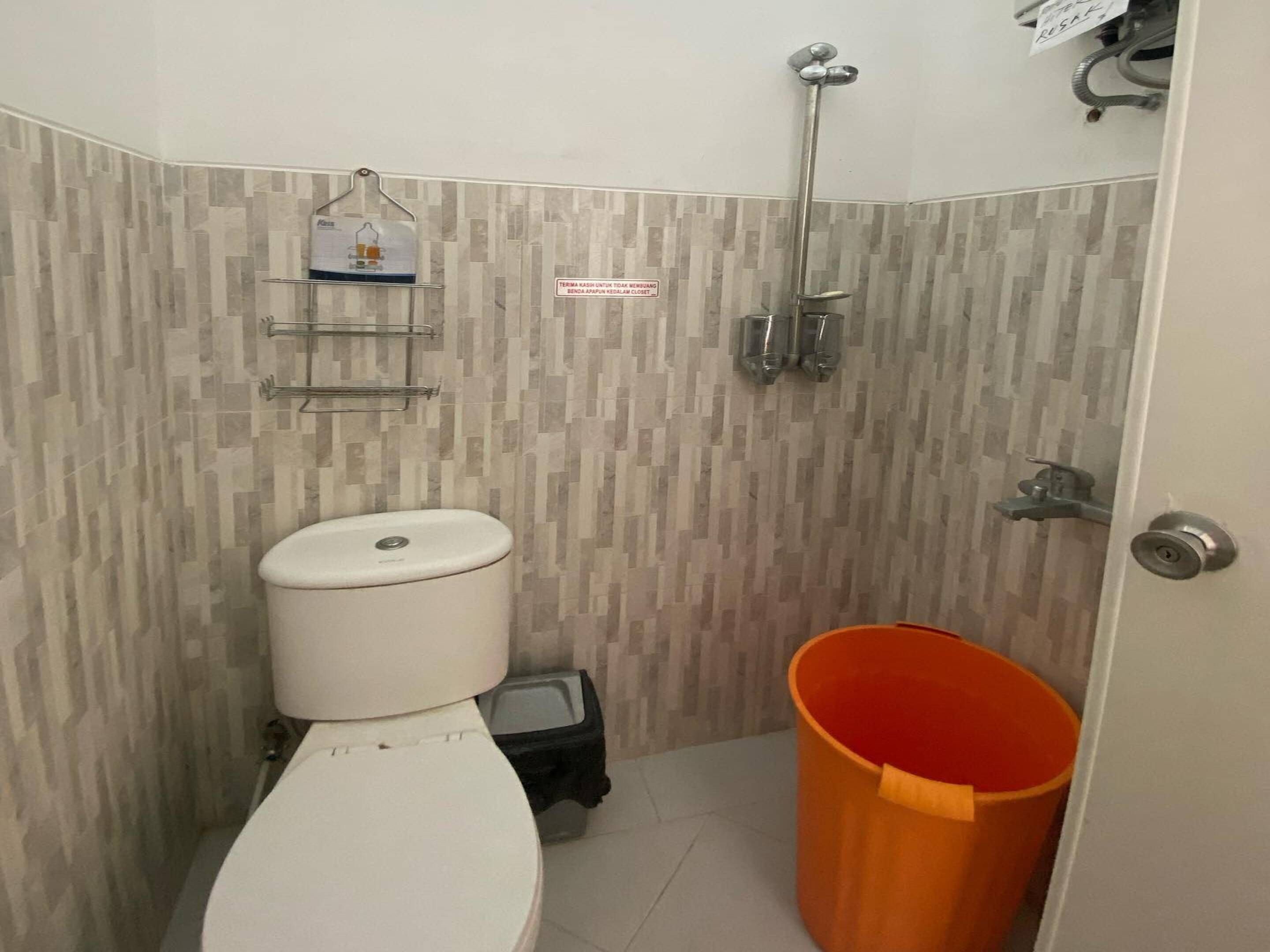 A bathroom with a toilet, a shower, and a waste bin.
