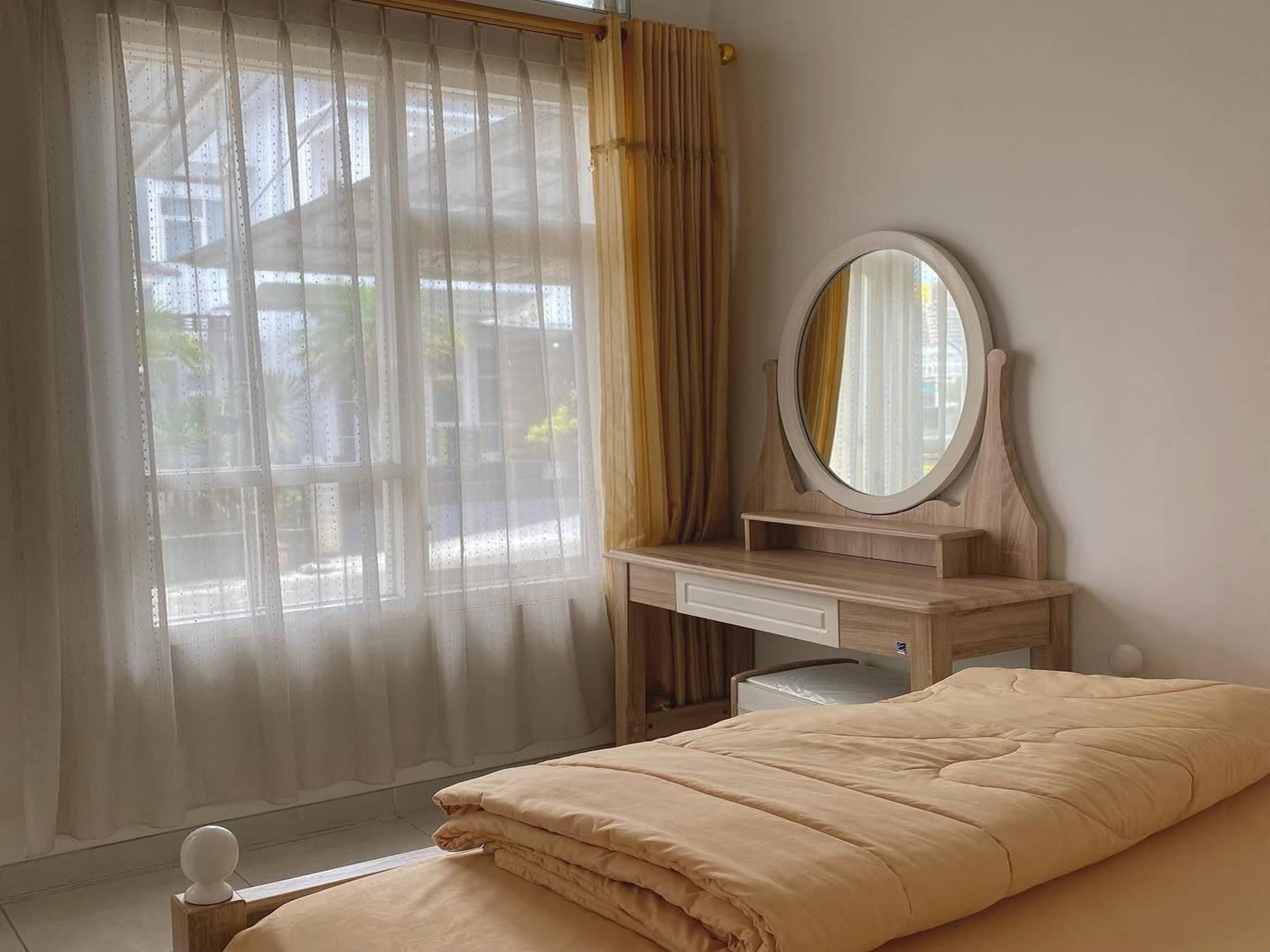 A bedroom with a bed, a wooden dresser, a mirror, and a window with curtains.
