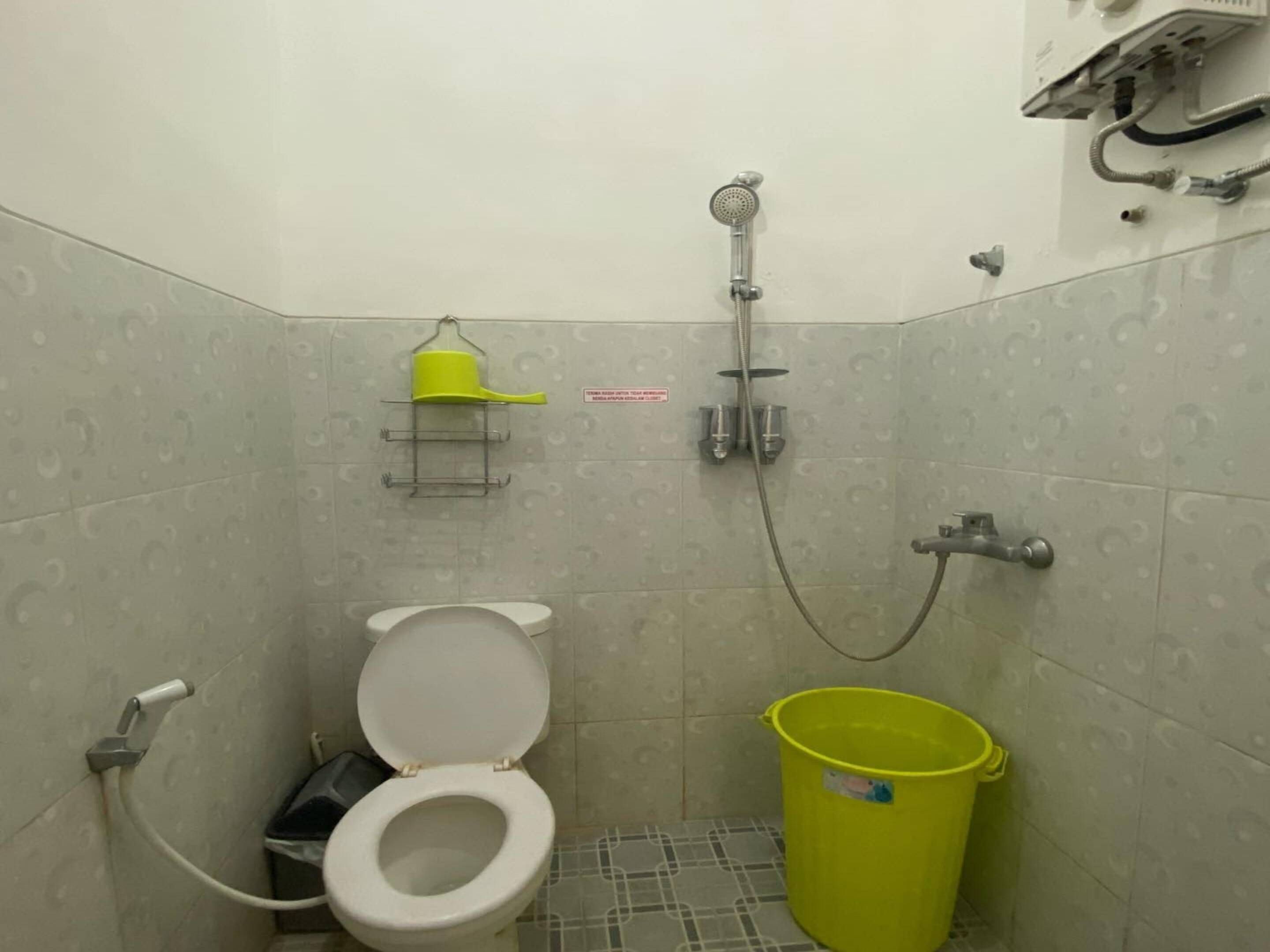 A small bathroom with a toilet, a shower, and a yellow bucket.