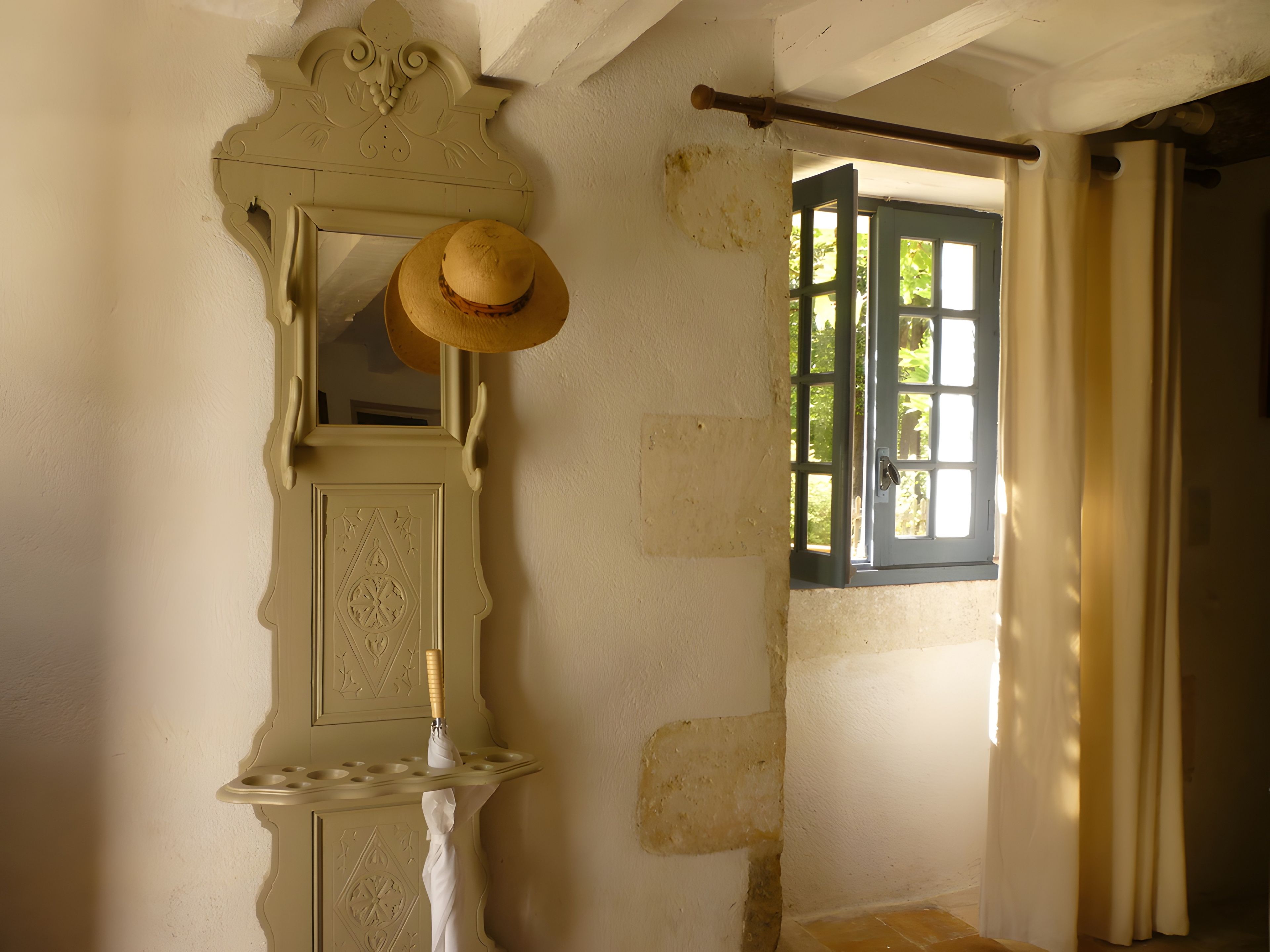 Una habitación con un espejo, un sombrero y una ventana con cortinas.