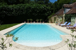 A rectangular swimming pool with a clear blue water surface, surrounded by a concrete deck. There are lounge chairs and potted plants along the poolside. - Country House 'Hameau des Rabauds - La Tourderie' with Pool, Private Garden & Wi-Fi (Saint-Pierre-de-Maillé)