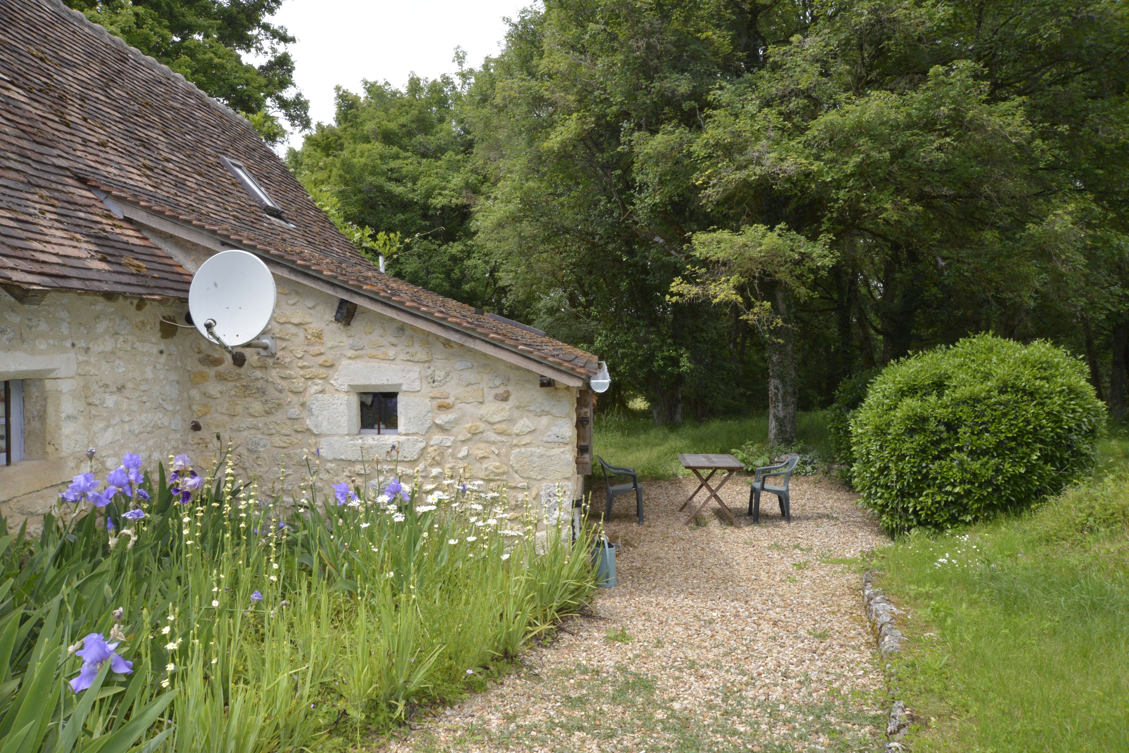 A stone house with a satellite dish, a gravel path, and a bench.