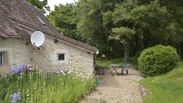 A stone house with a satellite dish, a gravel path, and a bench.
