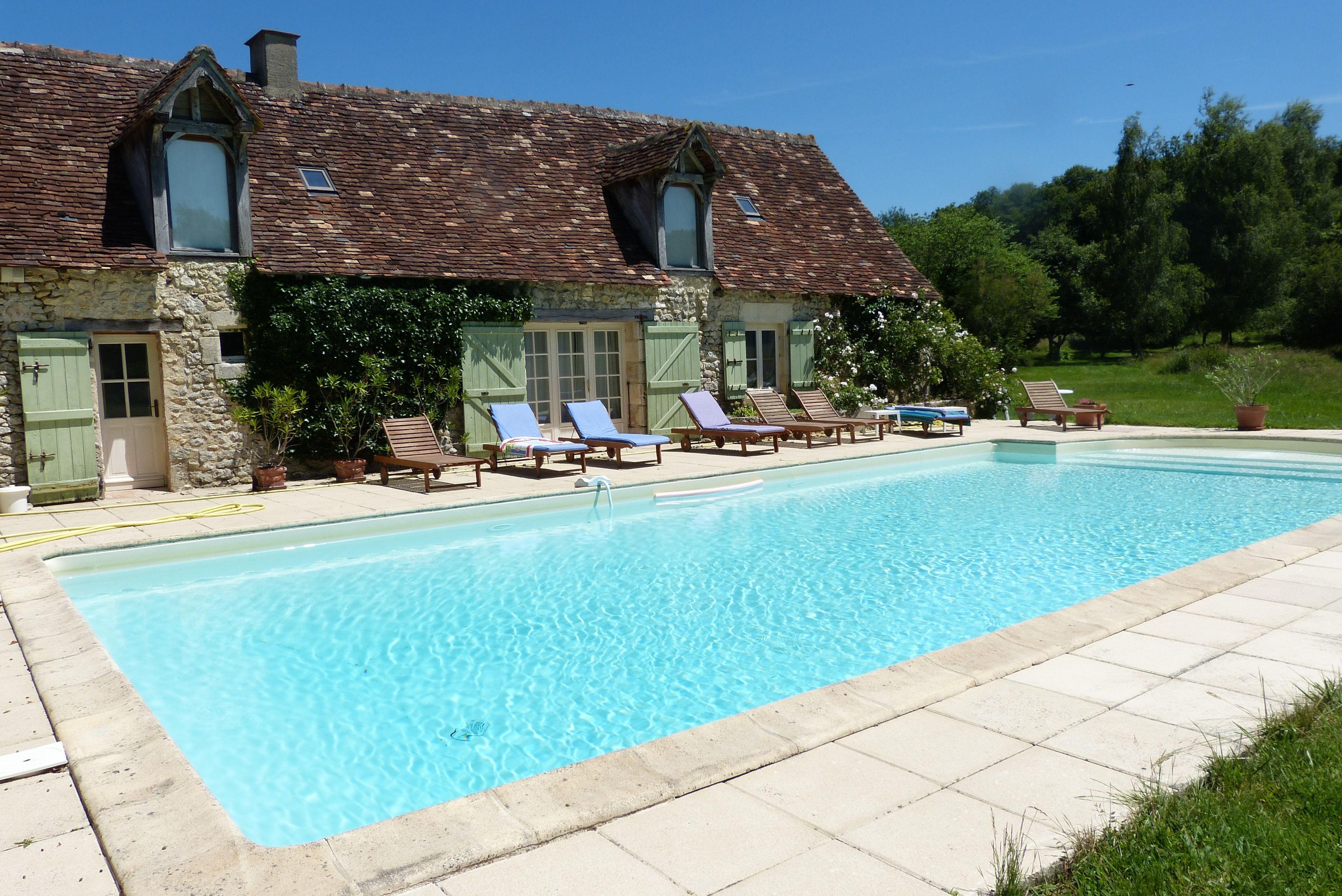 A stone building with a swimming pool, outdoor seating, and a natural backdrop.