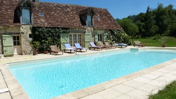A stone building with a swimming pool, outdoor seating, and a natural backdrop.
