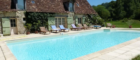 A stone building with a swimming pool, outdoor seating, and a natural backdrop.