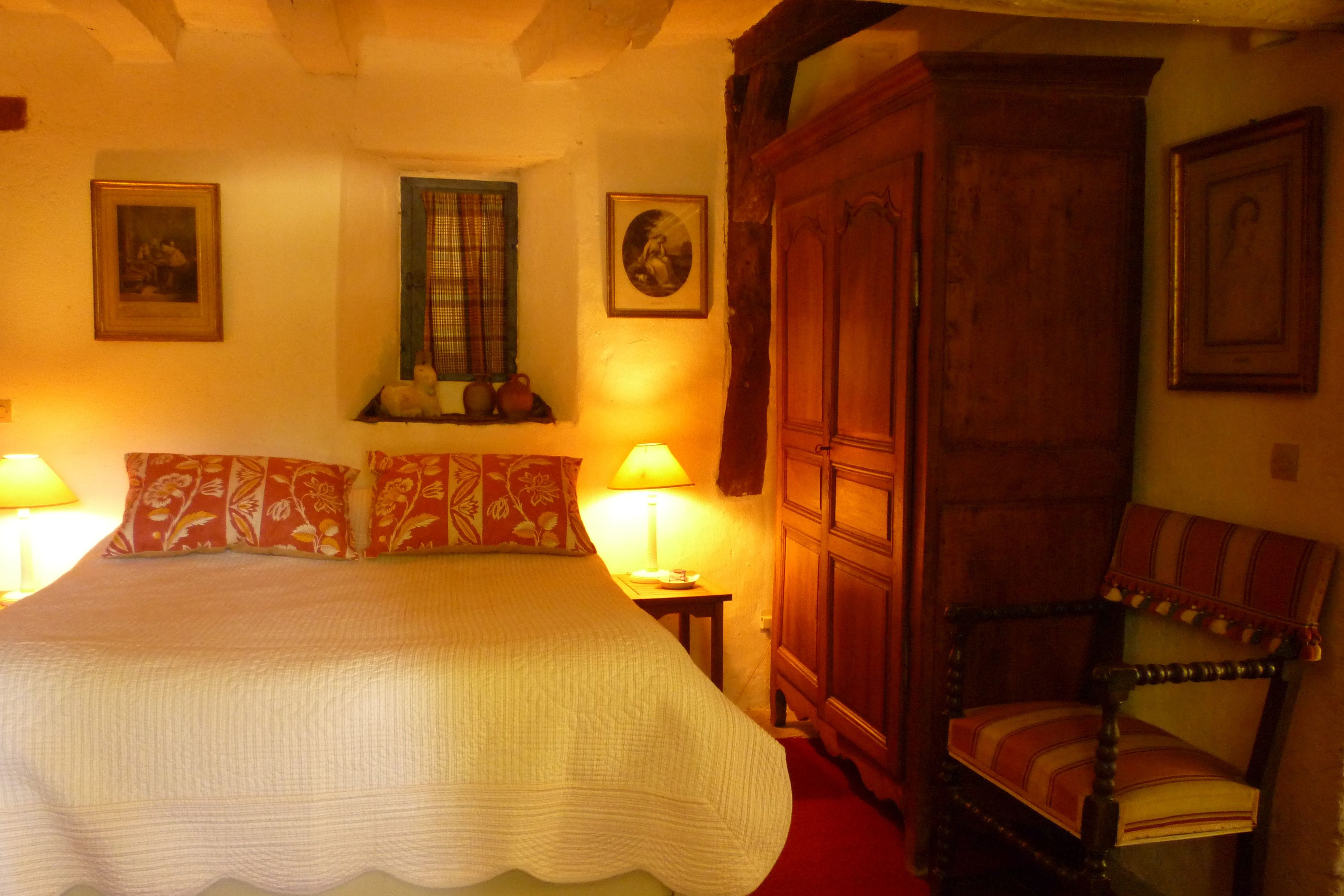 A bedroom with a large bed, a wooden wardrobe, a chair, and two bedside lamps.