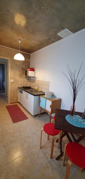 A compact kitchen with a dining area, a red rug, and a pendant light. - A-Tipica Guesthouse (Ponta Delgada)