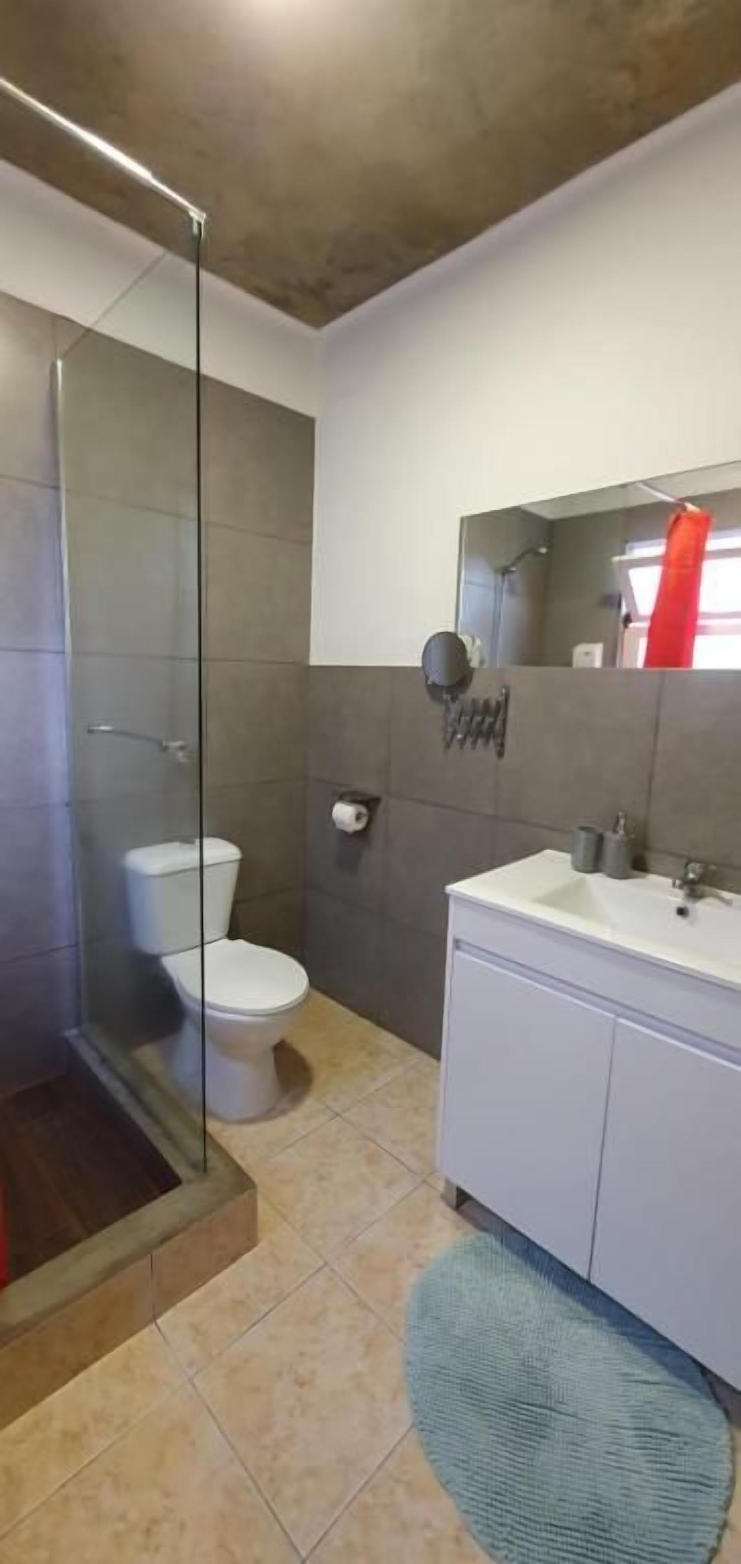 Un baño con ducha de vidrio, inodoro blanco y lavamanos con espejo.