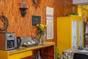 En frukostplats med en kaffemaskin, en vas med blommor och en griffeltavla som visar frukostens öppettider.