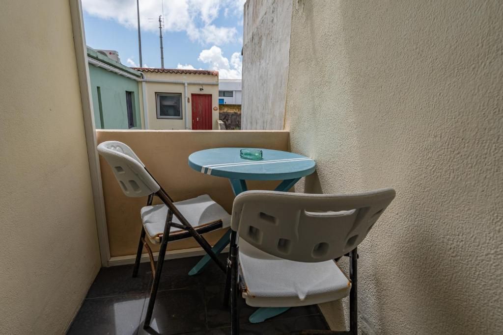 Un pequeño espacio al aire libre con dos sillas y una mesa, un estrecho pasaje entre edificios, y vista a un edificio con puerta roja.