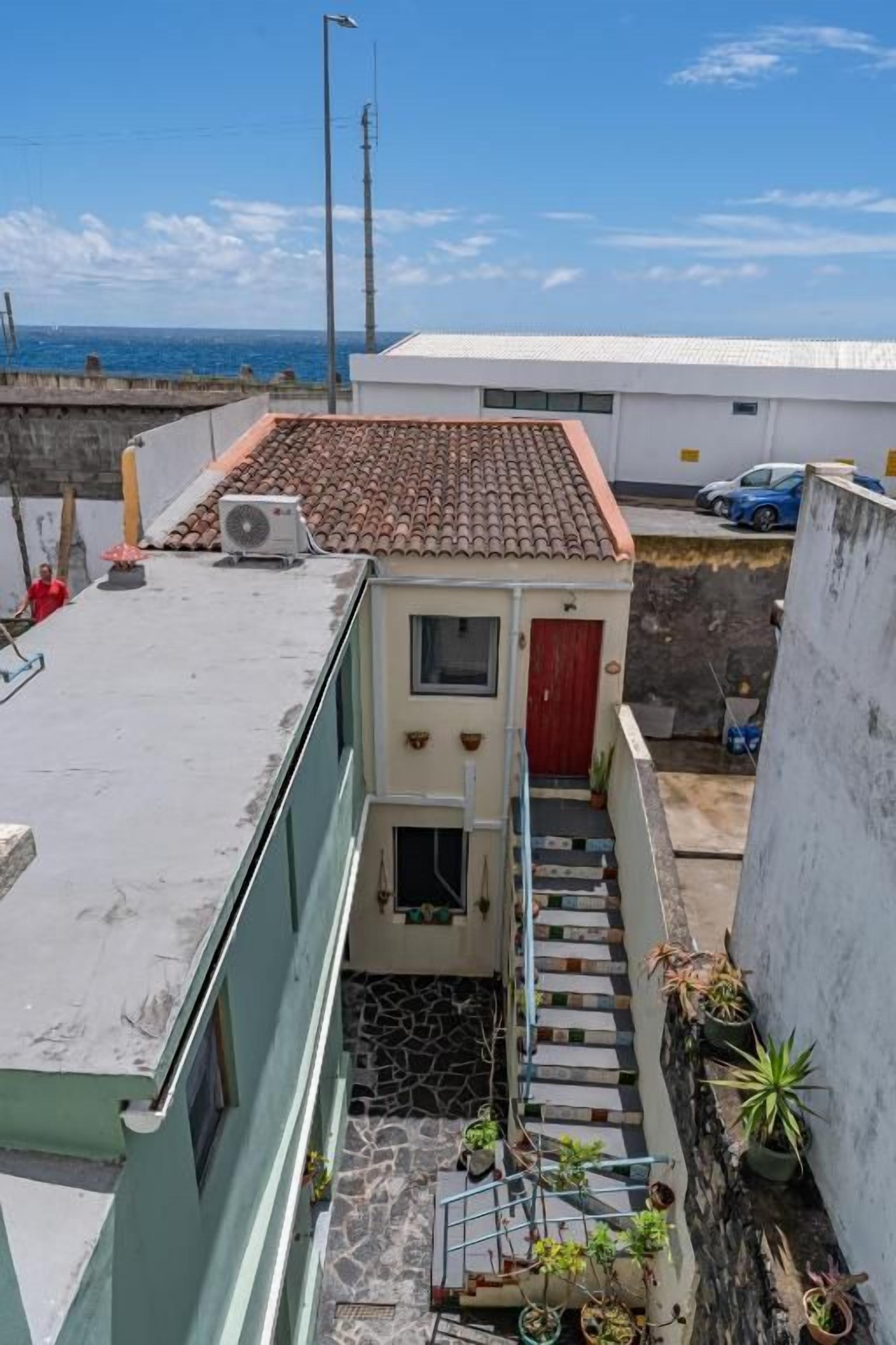 Edifício residencial com porta vermelha, pequena escadaria e vista para o mar.