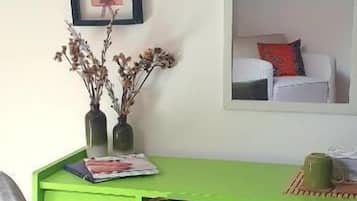 Una habitación con un escritorio verde, una silla, un cuadro enmarcado y un espejo que refleja una cama.