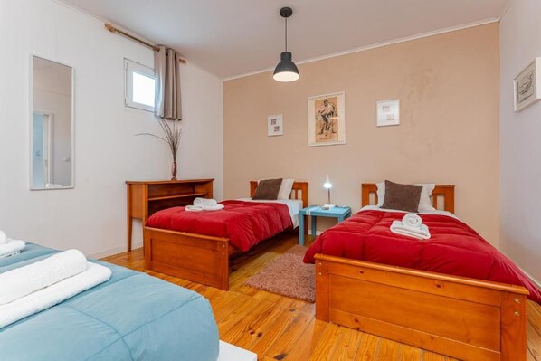A bedroom with two wooden beds, a small table, a mirror, and a window with curtains. - A-Tipica Guesthouse (Ponta Delgada)