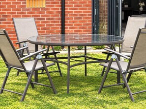 A round glass table with four chairs, set on a grassy lawn in front of a brick building. - 5 bedrooms| sleeps 12| Free parking| Garden (Walsall)