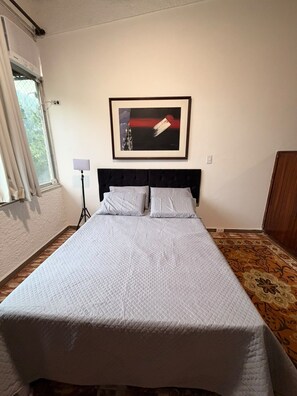 Ein Hotelzimmer mit einem Bett, einem gerahmten Kunstwerk an der Wand, einer Stehlampe und einem Fenster mit Vorhängen.