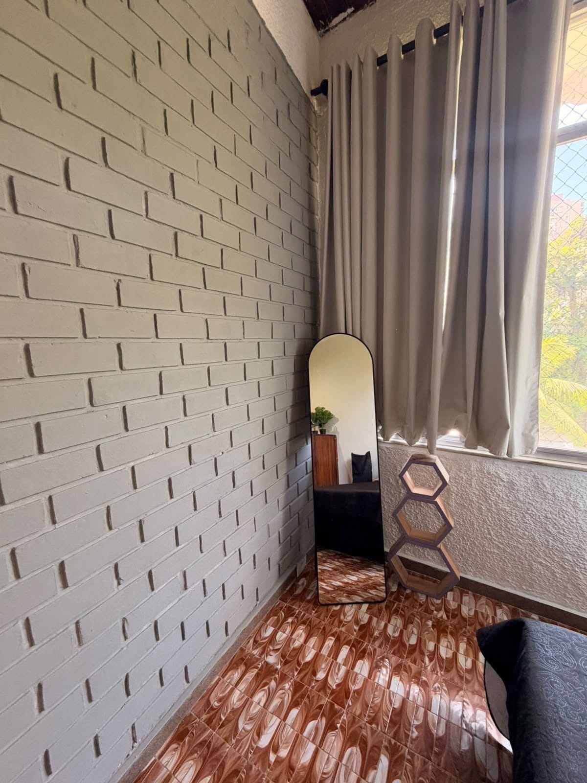 Une pièce avec un mur dont le motif imite des briques, un grand miroir, une fenêtre avec des rideaux et un sol à motifs.