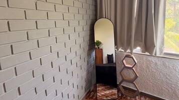 Une pièce avec un mur dont le motif imite des briques, un grand miroir, une fenêtre avec des rideaux et un sol à motifs.