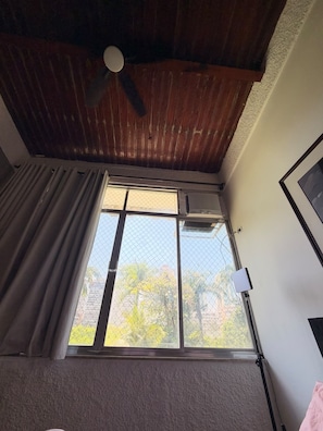 A room with a ceiling fan, a window with a view of trees, and a thermostat on the wall. - Seaside Retreat and Relaxation (Rio de Janeiro)