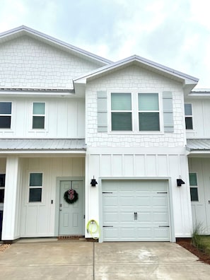 A two-story house with a garage, a front door with a wreath, and a driveway. - Brand new 3 bed/2.5 bath townhome central to the beach, Wharf, and restaurants! (Orange Beach)