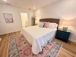 A bedroom with a large bed, a nightstand, a dresser, a rug, and a door leading to another room. - Brand new 3 bed/2.5 bath townhome central to the beach, Wharf, and restaurants! (Orange Beach)