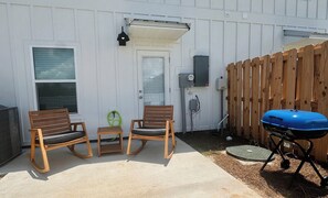 A patio with two rocking chairs, a small table, a grill, and a wooden fence. - Brand new 3 bed/2.5 bath townhome central to the beach, Wharf, and restaurants! (Orange Beach)