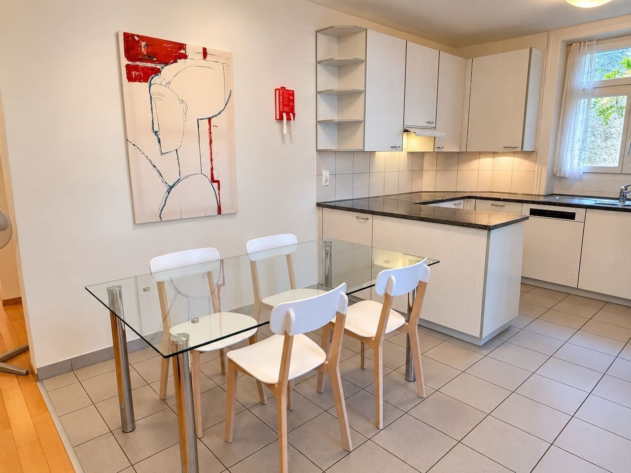 Cozinha moderna com armários brancos, uma mesa de jantar de vidro e uma pintura abstrata vermelha na parede.