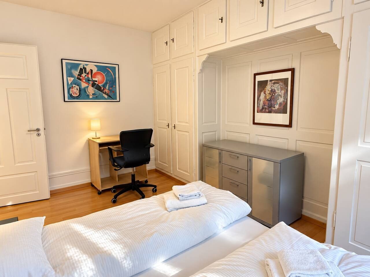 A hotel room with a bed, a desk, a chair, and a wardrobe.
