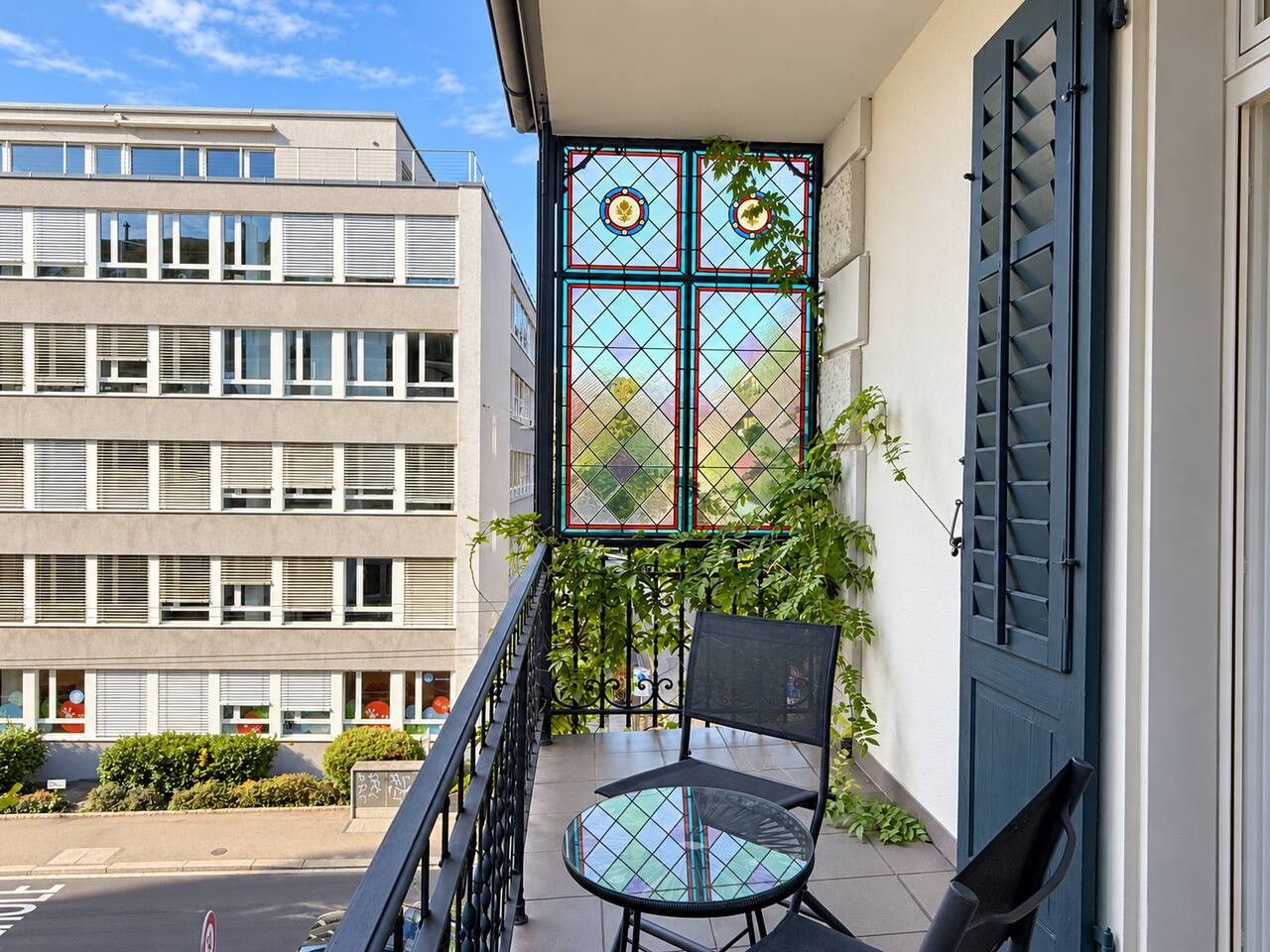 Ein Balkon mit einem Stuhl, eine blaue Tür und ein Gebäude mit mehreren Fenstern im Hintergrund.