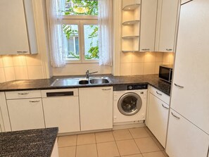 A compact kitchen with white cabinets, a washing machine, and a microwave. - Modern 2-Bedroom Apartment in the City Center - Hösch 10 (Zürich)