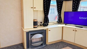 A room with a television, a fireplace, and a window with curtains. - Ingoldmells 2-bed Cabin, Sleeps 6 With Parking (Skegness)