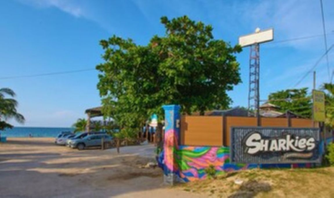 A beachfront property with a sign for 'Sharkies' and a view of the ocean.
