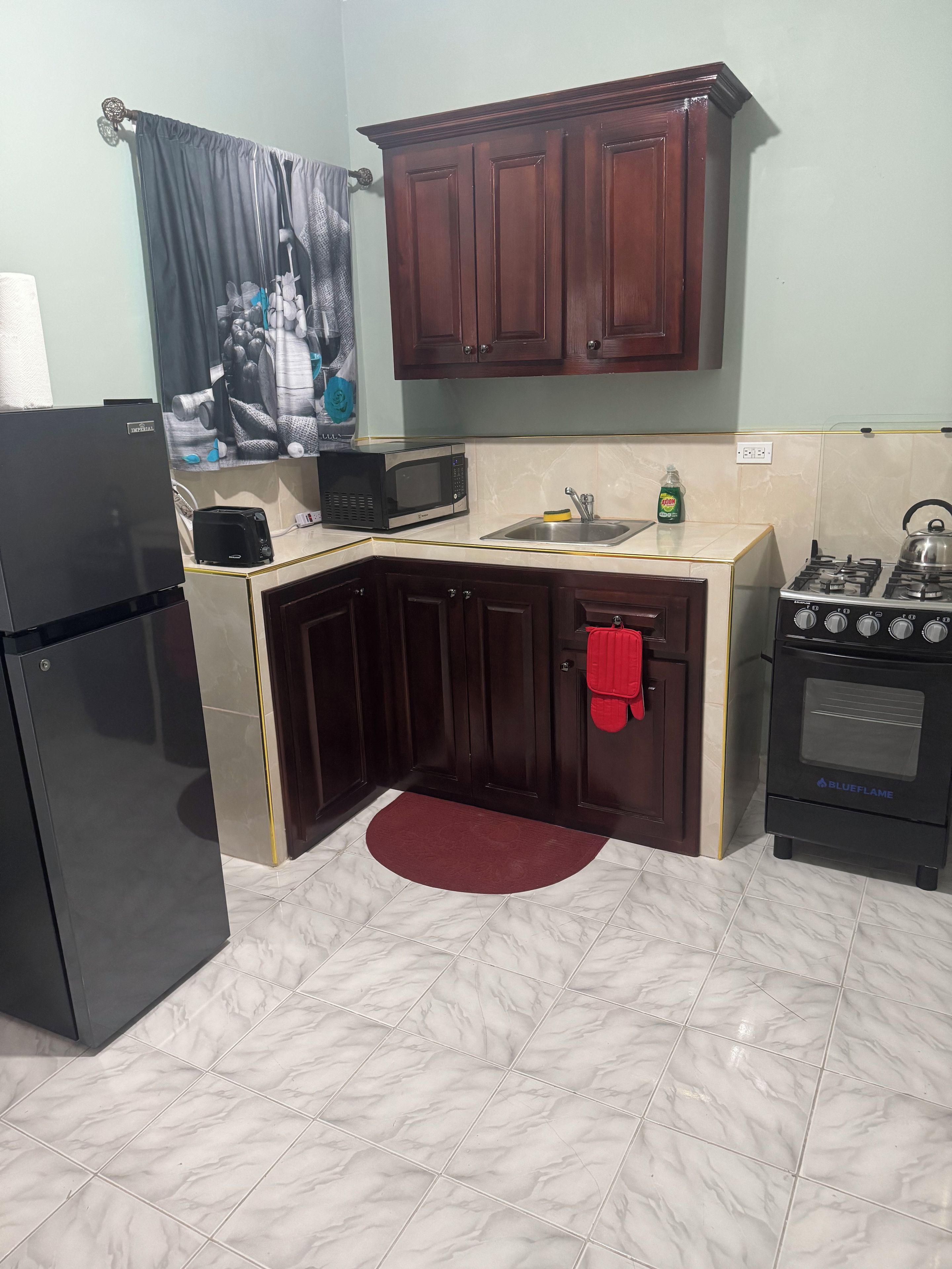 A compact kitchen with dark wooden cabinets, a black refrigerator, a microwave, a gas stove, and a sink.