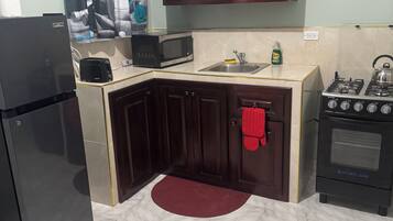 A compact kitchen with dark wooden cabinets, a black refrigerator, a microwave, a gas stove, and a sink.