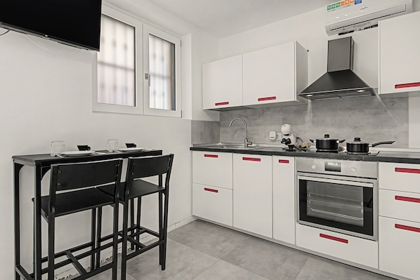 A modern kitchen with white cabinets, a black countertop, a built-in oven, and a dining area with a table and chairs. - Apartment 'Smart Hub M3 Metro 10 Min.Duomo' with shared garden, Wi-Fi and air conditioning (Milano)