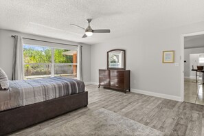 A bedroom with a bed, a dresser, a ceiling fan, and a large window. - Charming Kissimmee Retreat Near Orlando (Kissimmee)