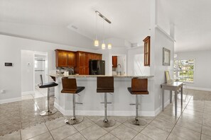 A modern kitchen with a central island, bar stools, and a dining table. - Charming Kissimmee Retreat Near Orlando (Kissimmee)