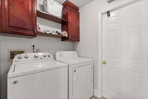 Une buanderie équipée d’un lave-linge et d’un sèche-linge Whirlpool, de placards en bois au-dessus du lave-linge et d’une porte blanche.