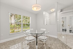Un coin repas avec une table et des chaises en verre, une fenêtre avec des stores et un luminaire au plafond.