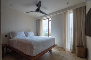 Une chambre à coucher avec un lit, un ventilateur de plafond, une fenêtre avec des rideaux et une vue sur les bâtiments à l’extérieur.
